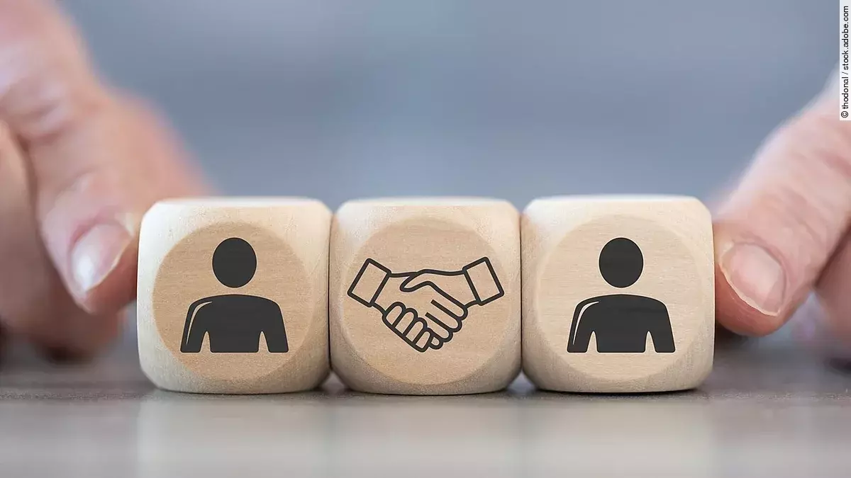 Deal Holzwürfel auf denen zwei Personen und ein Handschlag abgebildet sind.