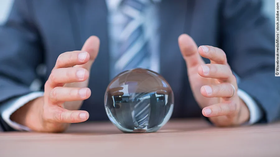 Vor einem Anzugträger liegt eine Glaskugel auf dem Tisch.