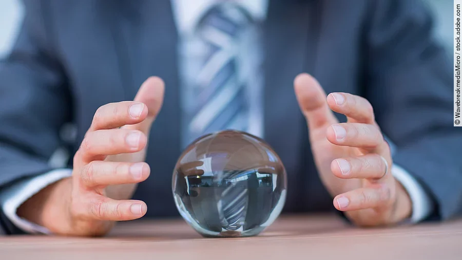 Vor einem Anzugträger liegt eine Glaskugel auf dem Tisch.