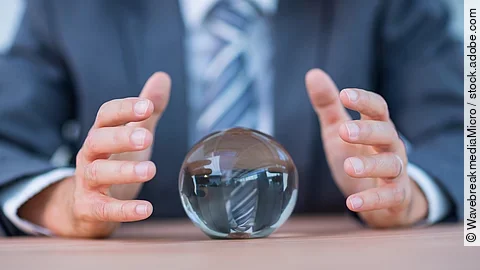 Vor einem Anzugträger liegt eine Glaskugel auf dem Tisch.