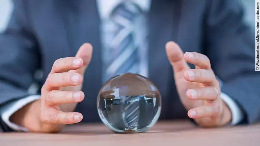 Vor einem Anzugträger liegt eine Glaskugel auf dem Tisch.