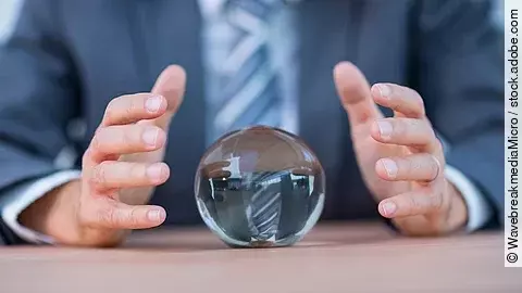 Vor einem Anzugträger liegt eine Glaskugel auf dem Tisch.