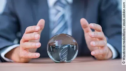 Vor einem Anzugträger liegt eine Glaskugel auf dem Tisch.