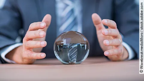 Vor einem Anzugträger liegt eine Glaskugel auf dem Tisch.