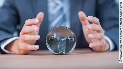 Vor einem Anzugträger liegt eine Glaskugel auf dem Tisch.