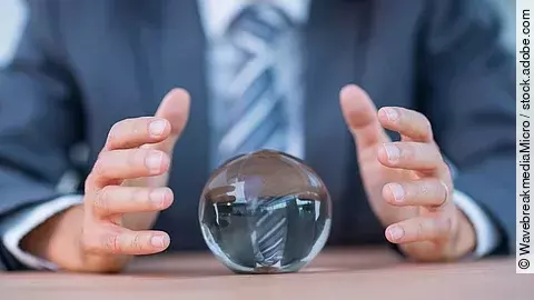 Vor einem Anzugträger liegt eine Glaskugel auf dem Tisch.