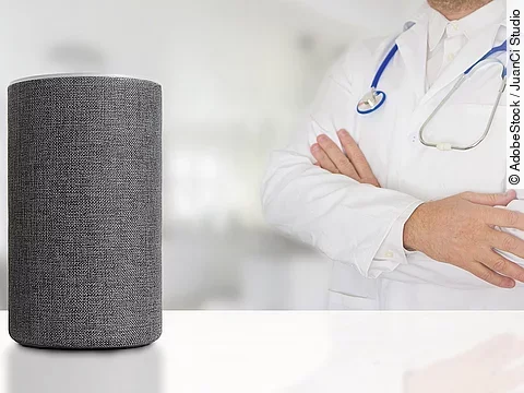 Sprachassistent Alexa steht auf weißem Untergrund. Dahinter wendet sich ein Arzt mit verschränkten Armen dieser Box zu.