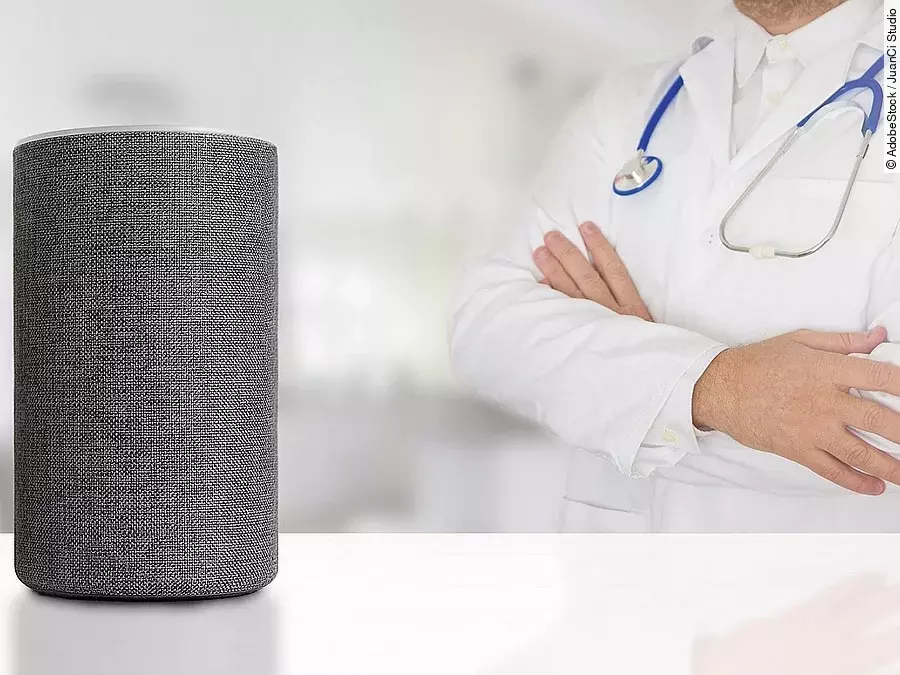 Sprachassistent Alexa Sprachassistent Alexa steht auf weißem Untergrund. Dahinter wendet sich ein Arzt mit verschränkten Armen dieser Box zu.