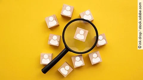 Mit einer Lupe mehrere Holzfiguren betrachten