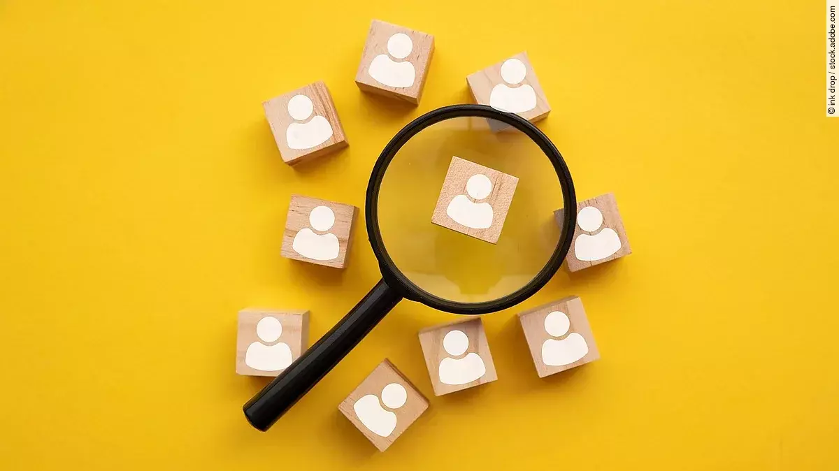 Mit einer Lupe mehrere Holzfiguren betrachten