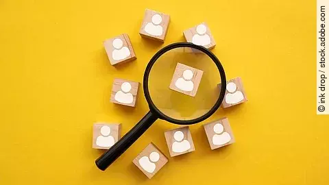 Mit einer Lupe mehrere Holzfiguren betrachten