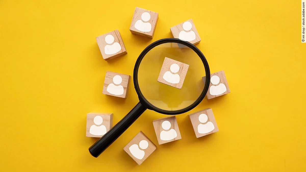 Mit einer Lupe mehrere Holzfiguren betrachten