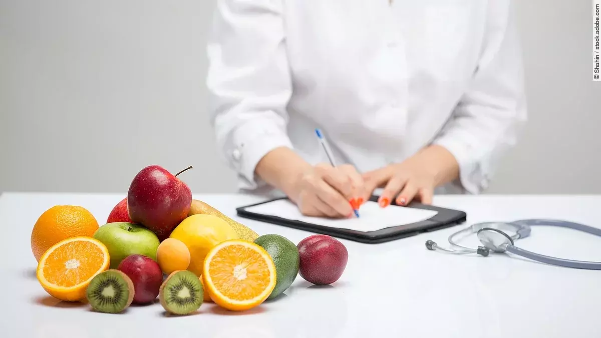 Obst liegt auf einem Tisch. Dahinter steht eine Frau, die etwas dokumentiert.