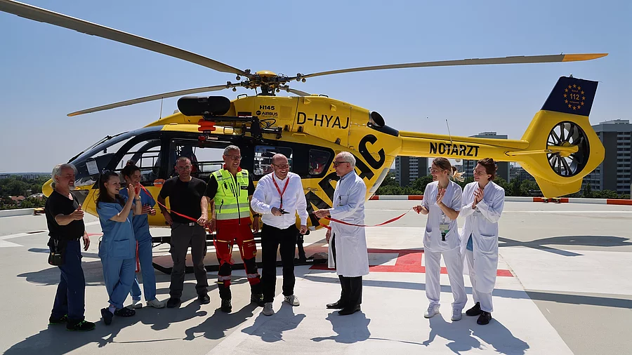 Menschen stehen vor einem gelben Helikopter und schneiden ein Band durch.