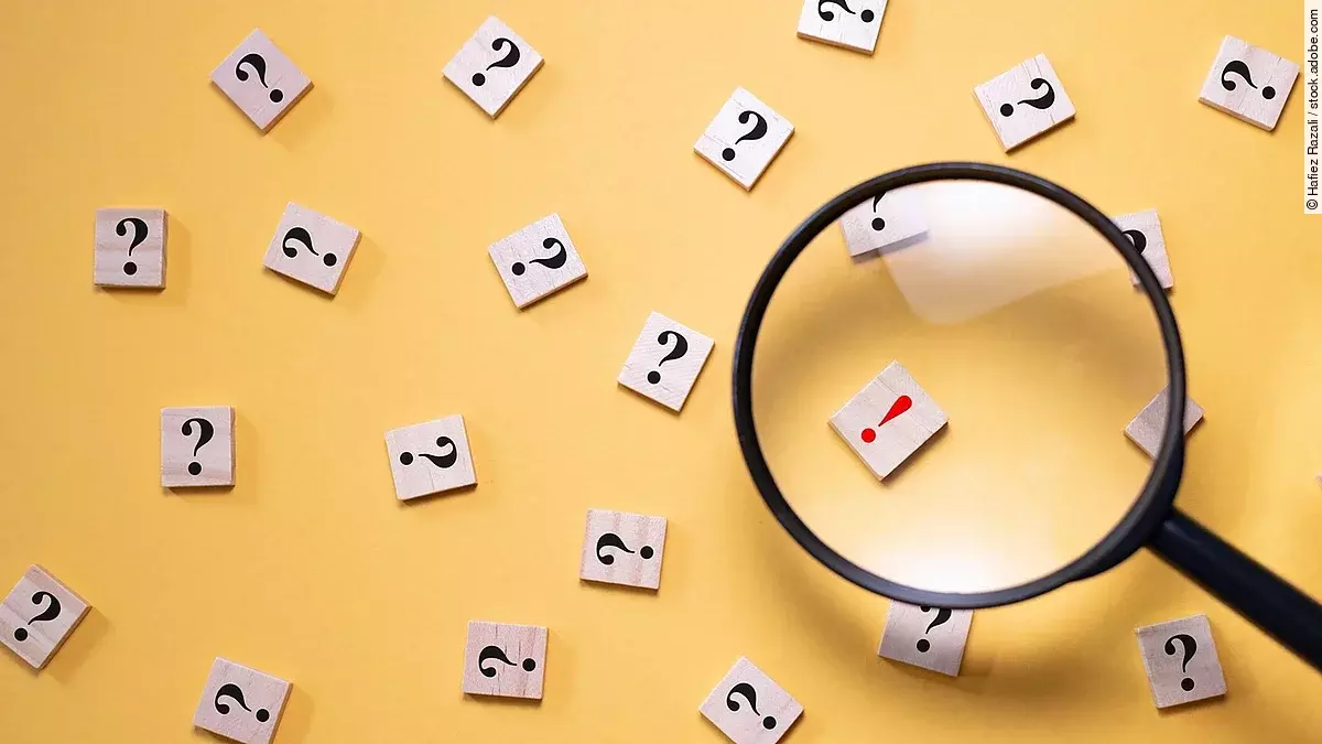 Viele Fragezeichen auf gelbem Hintergrund. Eine Lupe ist auf ein rotes Ausrufezeichen gerichtet