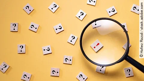 Plan Viele Fragezeichen auf gelbem Hintergrund. Eine Lupe ist auf ein rotes Ausrufezeichen gerichtet