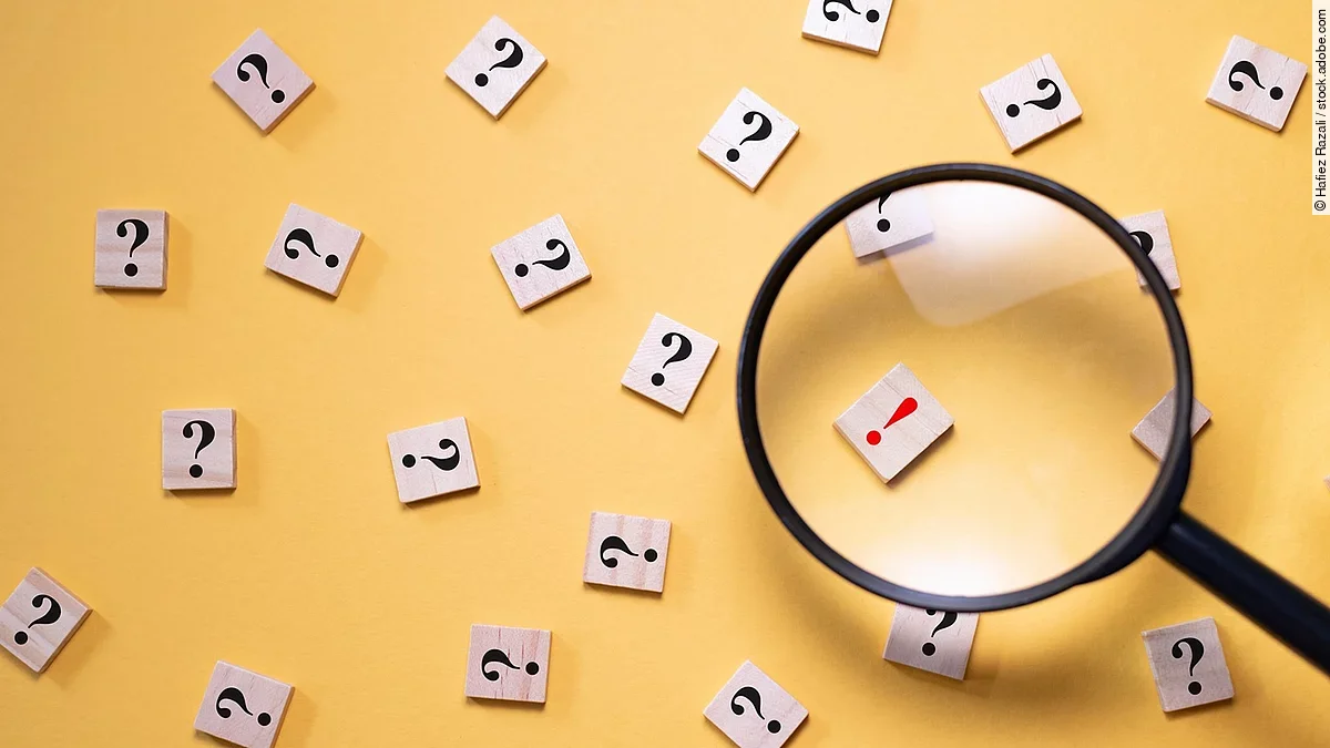 Viele Fragezeichen auf gelbem Hintergrund. Eine Lupe ist auf ein rotes Ausrufezeichen gerichtet