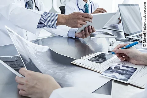Ärzte im Gespräch mit Röntgenaufnahmen und anderen Dokumenten.