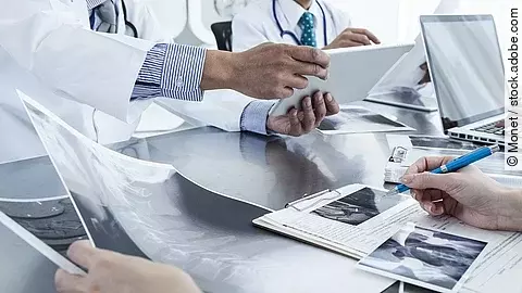 Ärzte im Gespräch mit Röntgenaufnahmen und anderen Dokumenten.