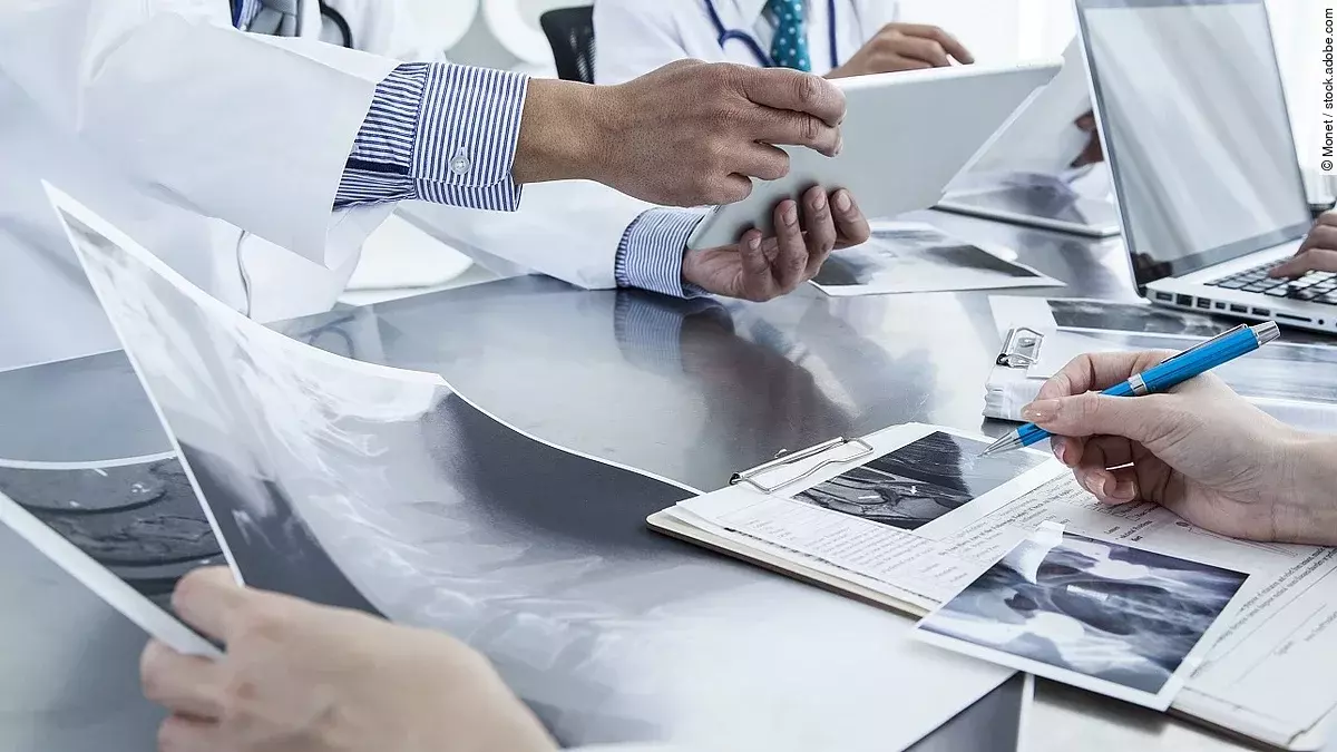 Ärzte im Gespräch mit Röntgenaufnahmen und anderen Dokumenten.