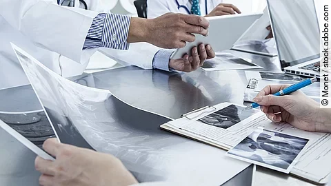 Ärzte im Gespräch mit Röntgenaufnahmen und anderen Dokumenten.