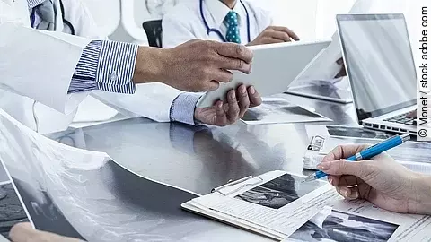 Ärzte im Gespräch mit Röntgenaufnahmen und anderen Dokumenten.