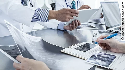 Ärzte im Gespräch mit Röntgenaufnahmen und anderen Dokumenten.