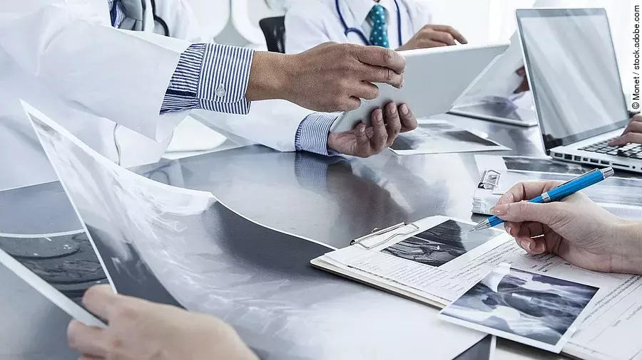 Ärzte im Gespräch mit Röntgenaufnahmen und anderen Dokumenten.