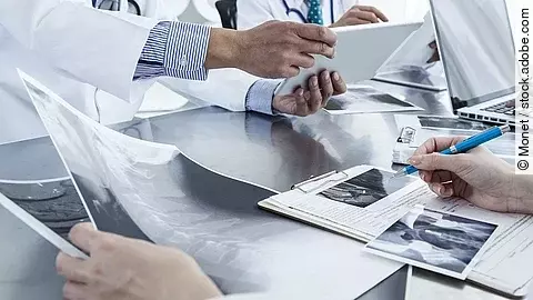 Ärzte im Gespräch mit Röntgenaufnahmen und anderen Dokumenten.