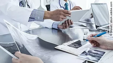 Ärzte im Gespräch mit Röntgenaufnahmen und anderen Dokumenten.