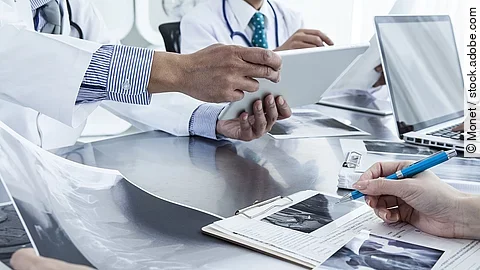 Ärzte im Gespräch mit Röntgenaufnahmen und anderen Dokumenten.