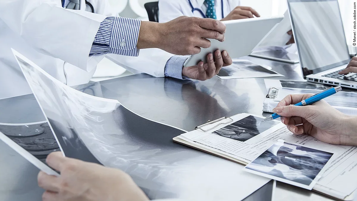 Ärzte im Gespräch mit Röntgenaufnahmen und anderen Dokumenten.