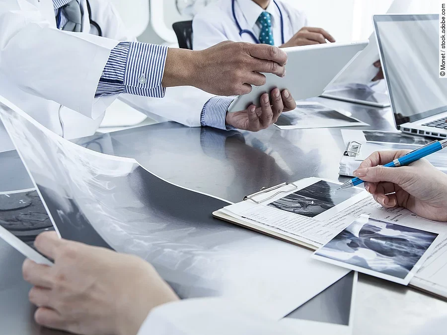 Ärzte im Gespräch mit Röntgenaufnahmen und anderen Dokumenten.