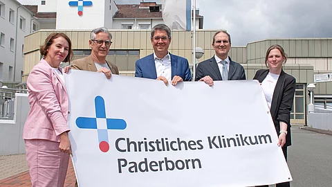 Brüderkrankenhaus St. Josef und Krankenhaus St. Johannisstift sind zum Christlichen Klinikum Paderborn fusioniert Fünf Menschen halten zusammen ein Poster hoch.