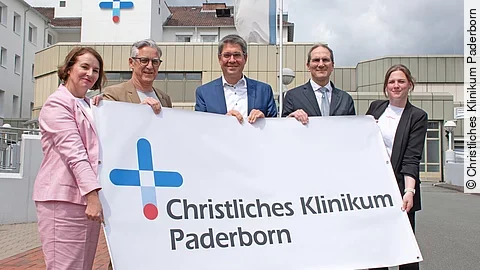 Brüderkrankenhaus St. Josef und Krankenhaus St. Johannisstift sind zum Christlichen Klinikum Paderborn fusioniert Fünf Menschen halten zusammen ein Poster hoch.