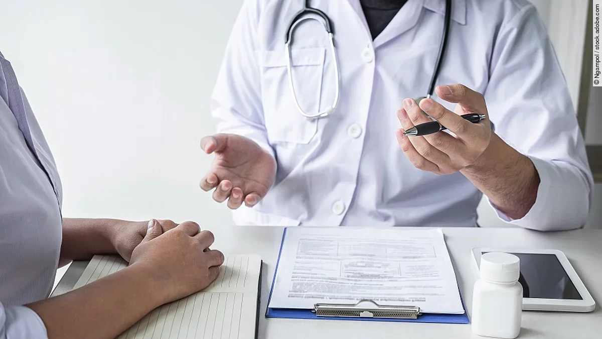 Arzt mit Patient Arzt sitzt seiner Patienten gegenüber und erklärt. Auf dem Tisch vor ihm liegen Dokumente und ein Wasserglas.