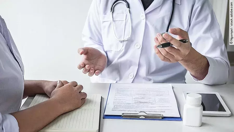 Arzt mit Patient Arzt sitzt seiner Patienten gegenüber und erklärt. Auf dem Tisch vor ihm liegen Dokumente und ein Wasserglas.
