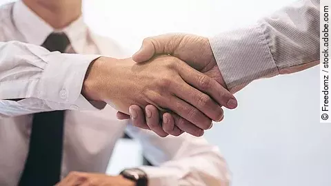 Händeschütteln Ein Mann mit Hemd und Krawatte sitzt an einem Tisch, vor ihm liegt ein Dokument und ein Stift. Er schüttelt die Hand eines anderen Mannes.