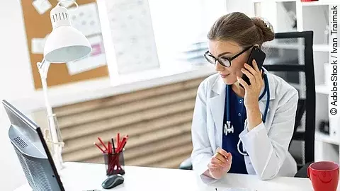 Ärztin am Telefon Ärztin sitzt an ihrem Schreibtisch und telefoniert. Vor ihr liegt eine Klemmmappe und ein Bildschirm.