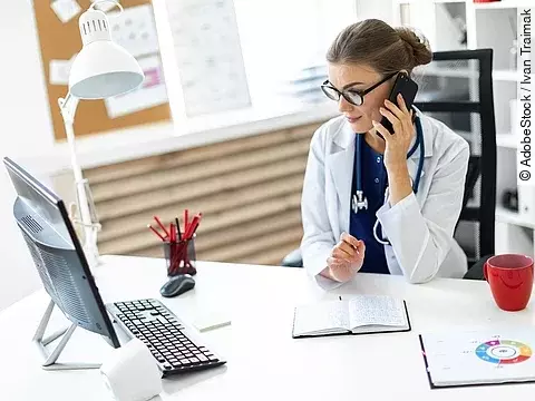 Ärztin am Telefon Ärztin sitzt an ihrem Schreibtisch und telefoniert. Vor ihr liegt eine Klemmmappe und ein Bildschirm.