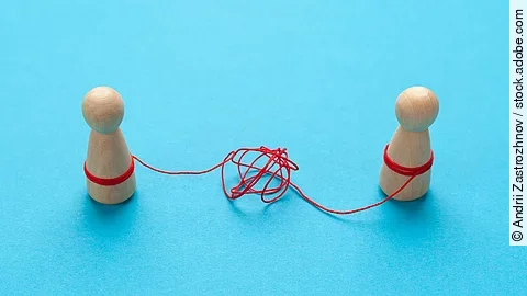 Streit Zwei Holz-Spielfiguren vor blauem Hintergrund stehen sich gegenüber und sind mit einer verknoteten roten Schnur verbunden.