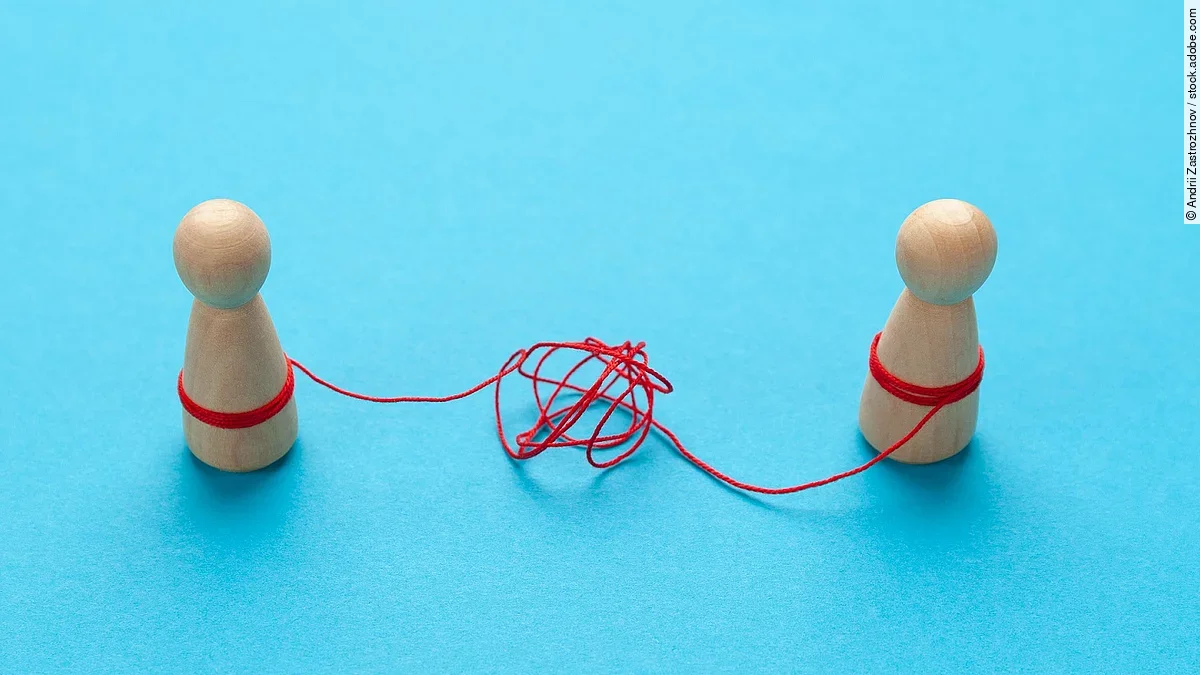 Streit Zwei Holz-Spielfiguren vor blauem Hintergrund stehen sich gegenüber und sind mit einer verknoteten roten Schnur verbunden.
