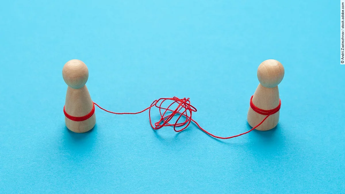Trennung Zwei Holz-Spielfiguren vor blauem Hintergrund stehen sich gegenüber und sind mit einer verknoteten roten Schnur verbunden.