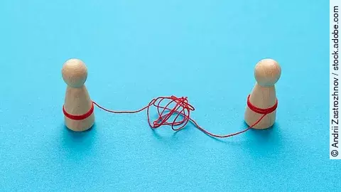 Trennung Zwei Holz-Spielfiguren vor blauem Hintergrund stehen sich gegenüber und sind mit einer verknoteten roten Schnur verbunden.