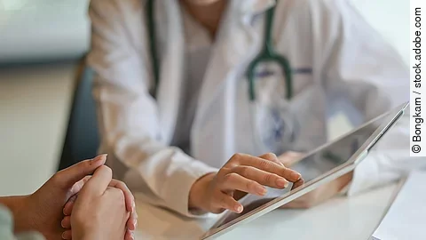 Arzt und Patient führen ein Gespräch. Der Arzt zeigt dem Patienten etwas auf dem Tablet.
