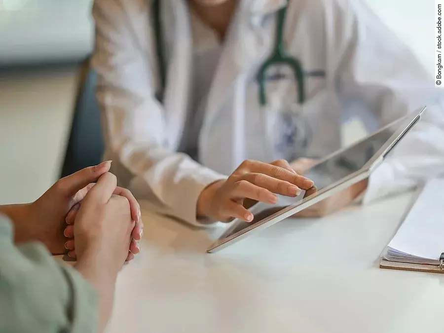 Arzt und Patient führen ein Gespräch. Der Arzt zeigt dem Patienten etwas auf dem Tablet.