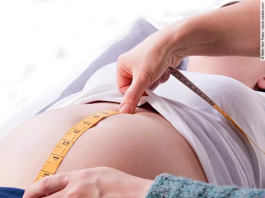 Zu sehen sind die Hände einer Hebamme, die den Bauch einer schwangeren Frau abmisst.