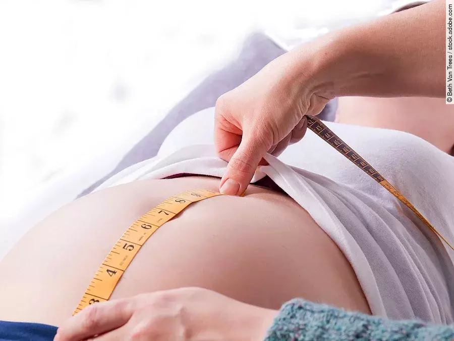 Zu sehen sind die Hände einer Hebamme, die den Bauch einer schwangeren Frau abmisst.