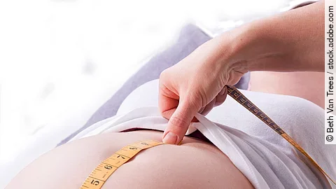 Zu sehen sind die Hände einer Hebamme, die den Bauch einer schwangeren Frau abmisst.