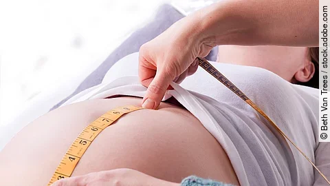 Zu sehen sind die Hände einer Hebamme, die den Bauch einer schwangeren Frau abmisst.